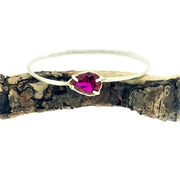 Full view of Ruby Shea Bangle. These bangles are all one-of-a-kind with a hand carved texture on the bangle, an unproportionable ovular shape, and one set gem on each bangle. On this bangle there is a set teardrop ruby. All made in sterling silver.