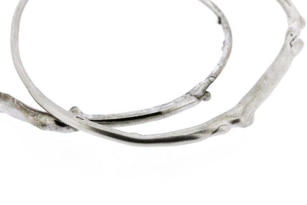 A detail photo of two sterling silver bangle bracelets that have a smooth organic texture that looks as if they are twigs covered in ice.