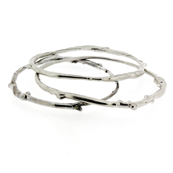 A set of three sterling silver bangle bracelets that have a smooth organic texture that looks as if they are twigs covered in ice.