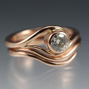 Rose Gold and Moissanite Engagement ring and nesting wedding band that have a vine or wave appearance.