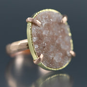 Angled view of Peach Druzy Chiseled Ring #2. The peach druzy is cut in an oval, set in gold with four rose gold prongs, laying on a rose gold chiseled band.