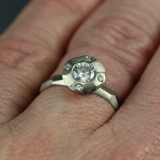 A contemporary halo style engagement ring on a woman's hand, featuring a center Moissante and 4 small stones in North, south, east west positions