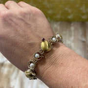 Sterling & 18k gold circle bracelet with pearls and garnet gemstones shown on a wrist.
