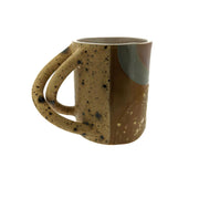 Full image of Criss Cross Mug. This mug has a variety of colors, including tan, white, cream and dark brown. The colors are separated by patches and dippings/drips. The handle of the mug is made of two handles that criss cross each other.