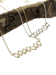 Close up view of two different White Topaz Cherin Necklace laying over a stick.