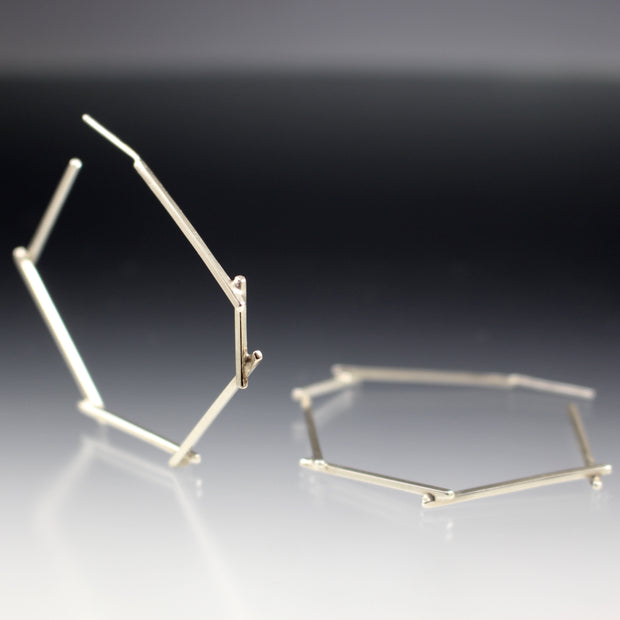 Angled view of Medium Stick Hoop Earrings with one standing up and the other laying flat.