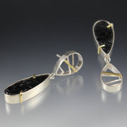 Full view of asymmetrical earing with black tourmaline. One is laying down on its side while the other is propped up.