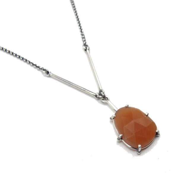 Detailed view of pendant on Peach Moonstone Necklace. There is a set peach moonstone at the base, set with six silver prongs attached to a silver bar that hangs from the Y of the necklace.