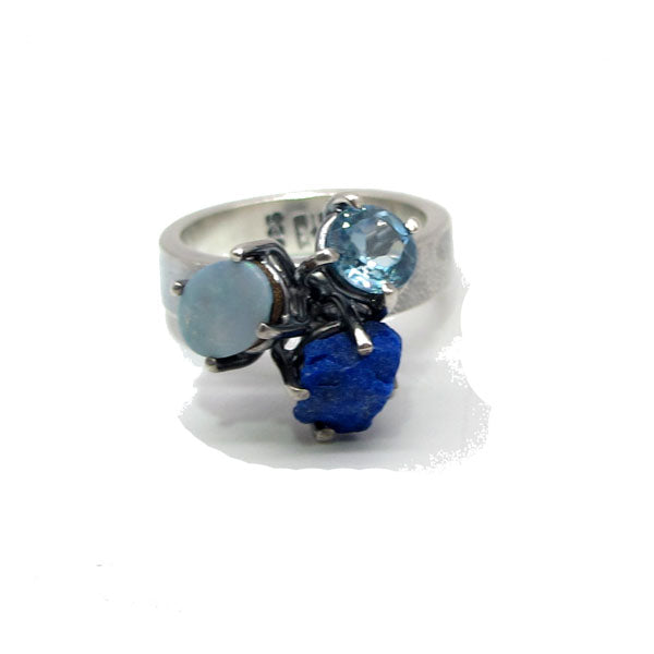 Frontal view of Triple Blue - Gemstone Ring. This ring has a thick silver band with three set gemstones at the top, Australian Opal doublet, rough lapis, blue topaz.
