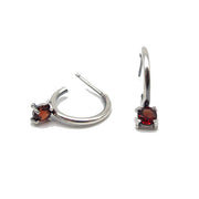 Full view of Garnet Tiny Hoop Earrings. These hoop earrings are made of silver and have a set piece of garnet attached to its base.