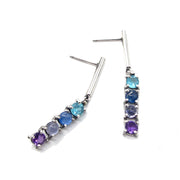 Full view of BIV - Drop Earrings. These earrings showcase a silver bar at the top and attached to the bar are three set gems, one after another, apatite, kyanite, iolite, amethyst.