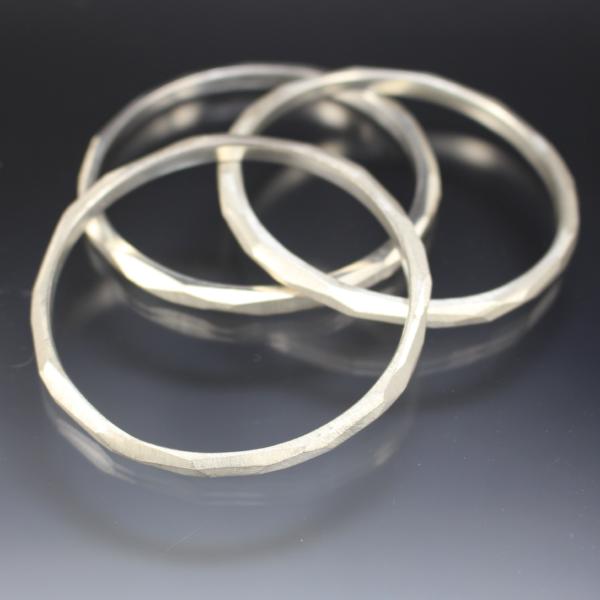 A cluster of three sterling silver bangle bracelets that have a faceted texture.
