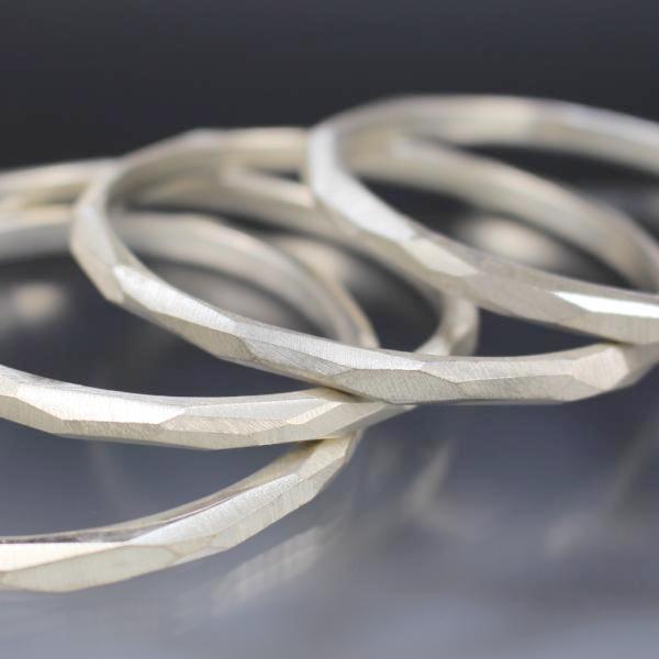 A stack of sterling silver bangle bracelets that have a faceted texture.