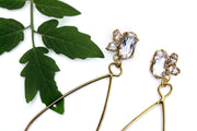 Detail photo of the top section of a pair of gold earrings a cluster of three white topaz gemstone set in an organic prong setting with a plant in the background.