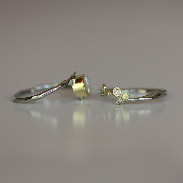 mixed metal engagement ring set in bypass style.  Bezel set moissanite in 18k yellow gold is flanked by 14k white gold.  Band features 18K gold dots with diamonds flush set. 