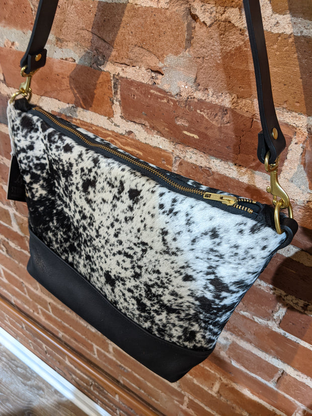 Angled view of Virginia shoulder bag in black and white cowhide. This view showcases the brass zipper on the bag.