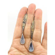 Full frontal image of Fused Lichen Sprout Dendritic Agate Dramatic Long Drop Earrings with hand in background to give an idea of the scale of the piece.