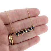 Close up view of Sapphire Cherin necklace draped over woman's hand to help give an idea of its scale.