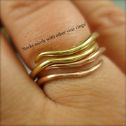 Two wave-like rings stacked together on a woman's finger, one is yellow gold and one is rose gold