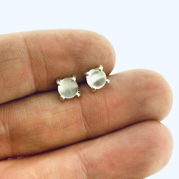 Full view of clear small round cabochon stud earrings in-between two fingers to help give idea of scale of piece.