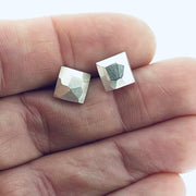 Full view of square faceted stud earrings in-between two fingers to give idea of scale of piece.