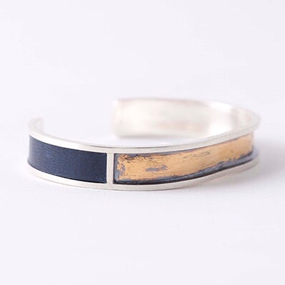 Full view of T.K. Cuff in navy leather. This cuff is made of silver and split into three rectangles. the two side rectangles are filled with the blue leather and the middle rectangle is oxidized silver with brushed on gold.