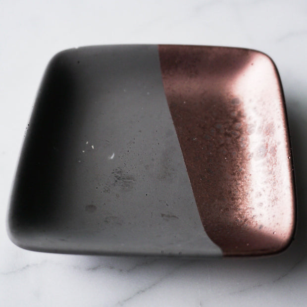 Full image of square concrete jewelry dish with a third of it dipped diagonally in copper paint.