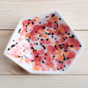 Full image of porcelain geometric ring dish with poppy design on top of a white finish. Red and orange create the petals and black creates the seeds of the poppy. 