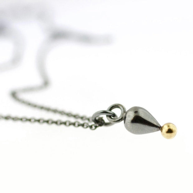 Close up view of Plumb Drop large Pendant. This pendant showcases a sculptural teardrop of oxidized silver and a gold ball at the tip.