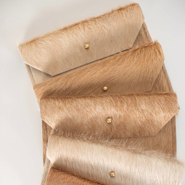 Full image of four stacked phone clutch's in blonde cowhide (a variety of light tan). It has an accent of brass button that helps open and close clutch.