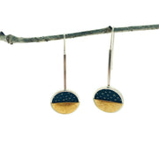W.N. Earrings on a white background. These dangle earrings are of a circle that the bottom half is if gokd and top black learher with textured dots. 