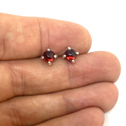 Full view of red small round cabochon stud earrings in-between two fingers to help give idea of scale of piece.