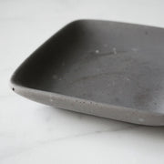 Close up view of square grey concrete jewelry dish.