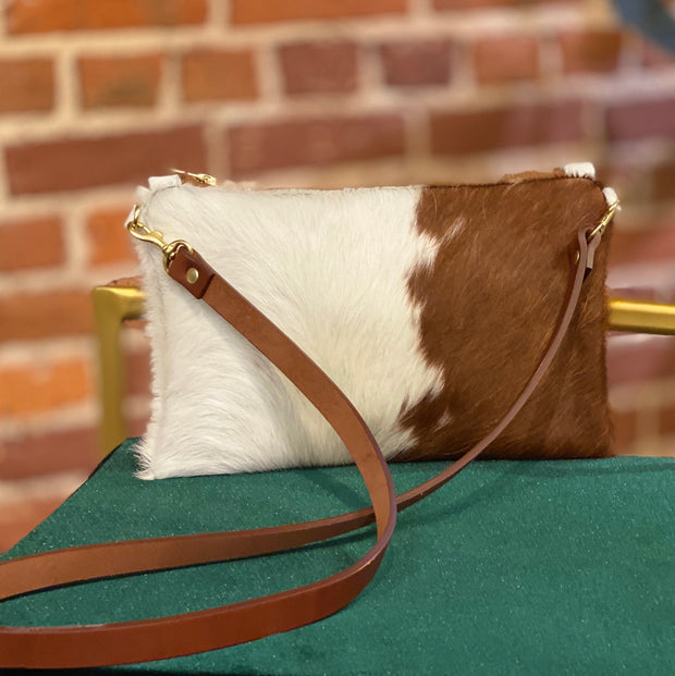 Full image of Wylie cross body bag in a brown and white cowhide with brown strap, sitting on top of a chair.