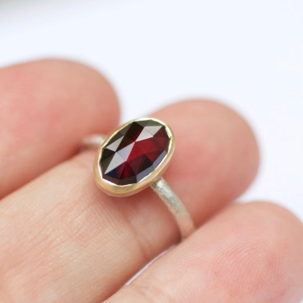 Full view of Luxe Stacking Ring - Garnet Rose Cut on woman's hand to help give an idea of its scale. An ovular shaped garnet bezel set in gold and laying on a silver band.