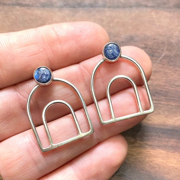 Full view of Melody Bow - Kyanite Earrings in-between fingers to help give idea of scale of piece.