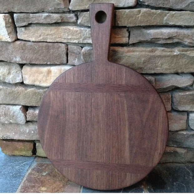 Full view of 12" Round Walnut Cutting Board with Inlay. In the shape of a circle with a handle, there is an inlay of an opposing design within the center part of the cutting board.