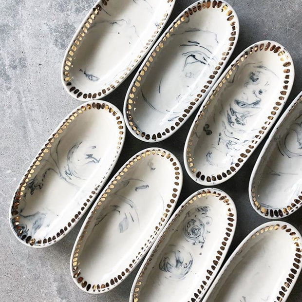 Full view of several Black Marbling oval dishes with gold dashes outlining the ridges.