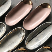 Full image of several oval dishes all next to one another in a variety of colors (pink, gold, black and white) and designs.