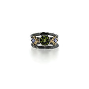 Full view of Solis Ring. Her center stone is a bright, sparkly Peridot that is an intense shade of lime green.  Surrounding her are a pair of brilliant purple princess cut Tanzanites in 14K Yellow gold bezels.  She's capped by two Sterling Silver Bands with just enough black patina in the recessed areas.  