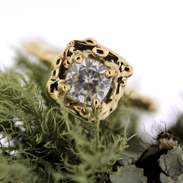 Close up view of diamond on Jordan Ring with moss in background. Details are carefully and individually sculpted around a beautiful cushion shaped diamond center stone, and no two iterations are ever exactly alike.  Prong set with an organically carved metal halo in a softened square shape surrounding the diamond.