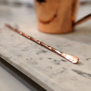 Full view of Copper Cocktail Stirrer. made entirely of copper, it has a twisted handle and hammered texture for the flat tip.