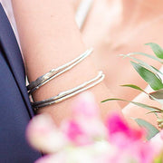 A detail photo of a woman's arm wearing a stack of sterling silver bangle bracelets that have a smooth organic texture that looks as if they are twigs covered in ice.