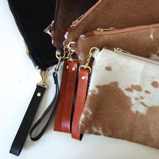 Full image of five different leather wrist straps for cowhide purses on their respective purse to give idea of scale. They come in brown or black. 